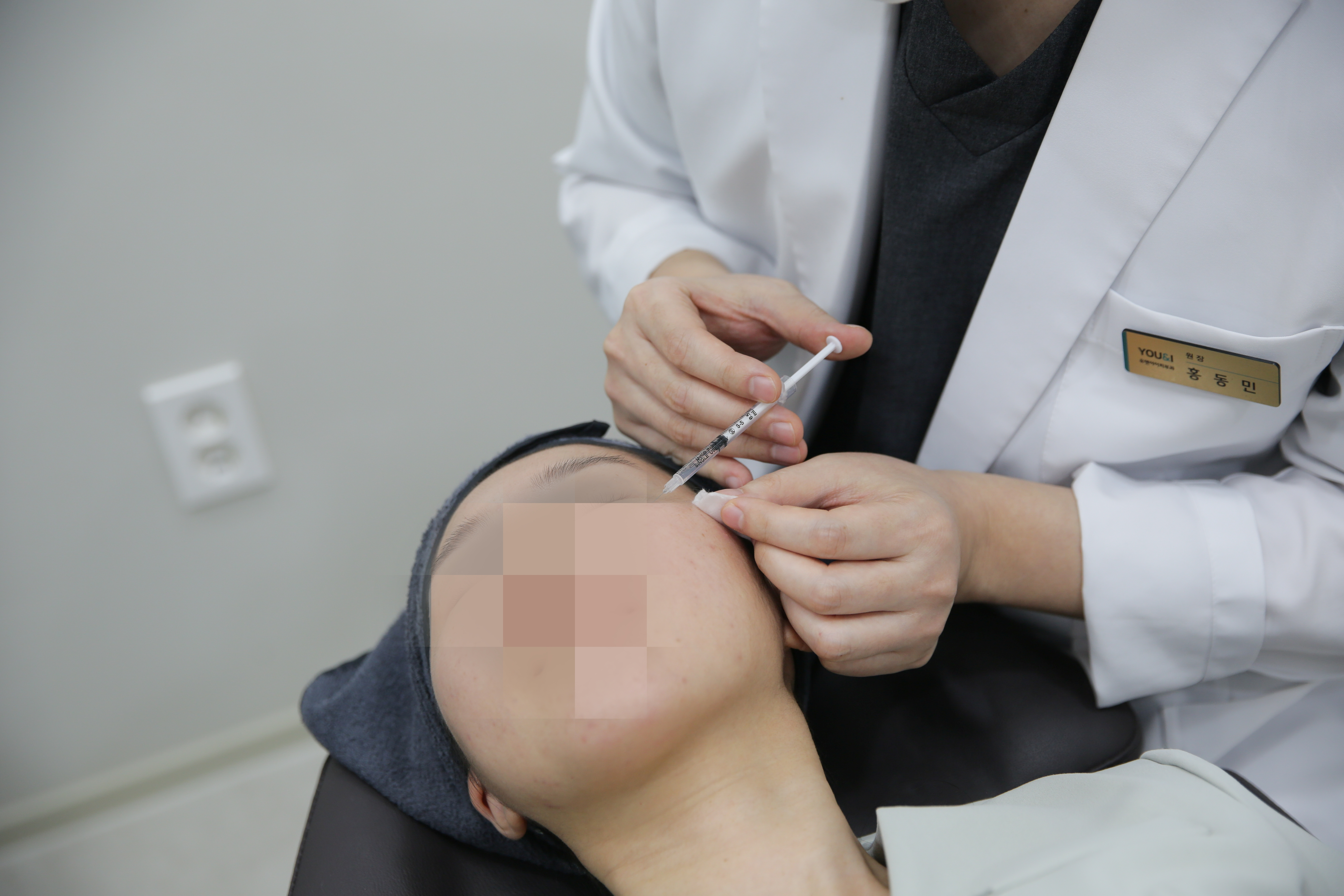 유앤아이의원 부산점 의료진이 진료실에서 환자의 눈썹 주변 얼굴 부위에 주사 시술을 진행하는 모습