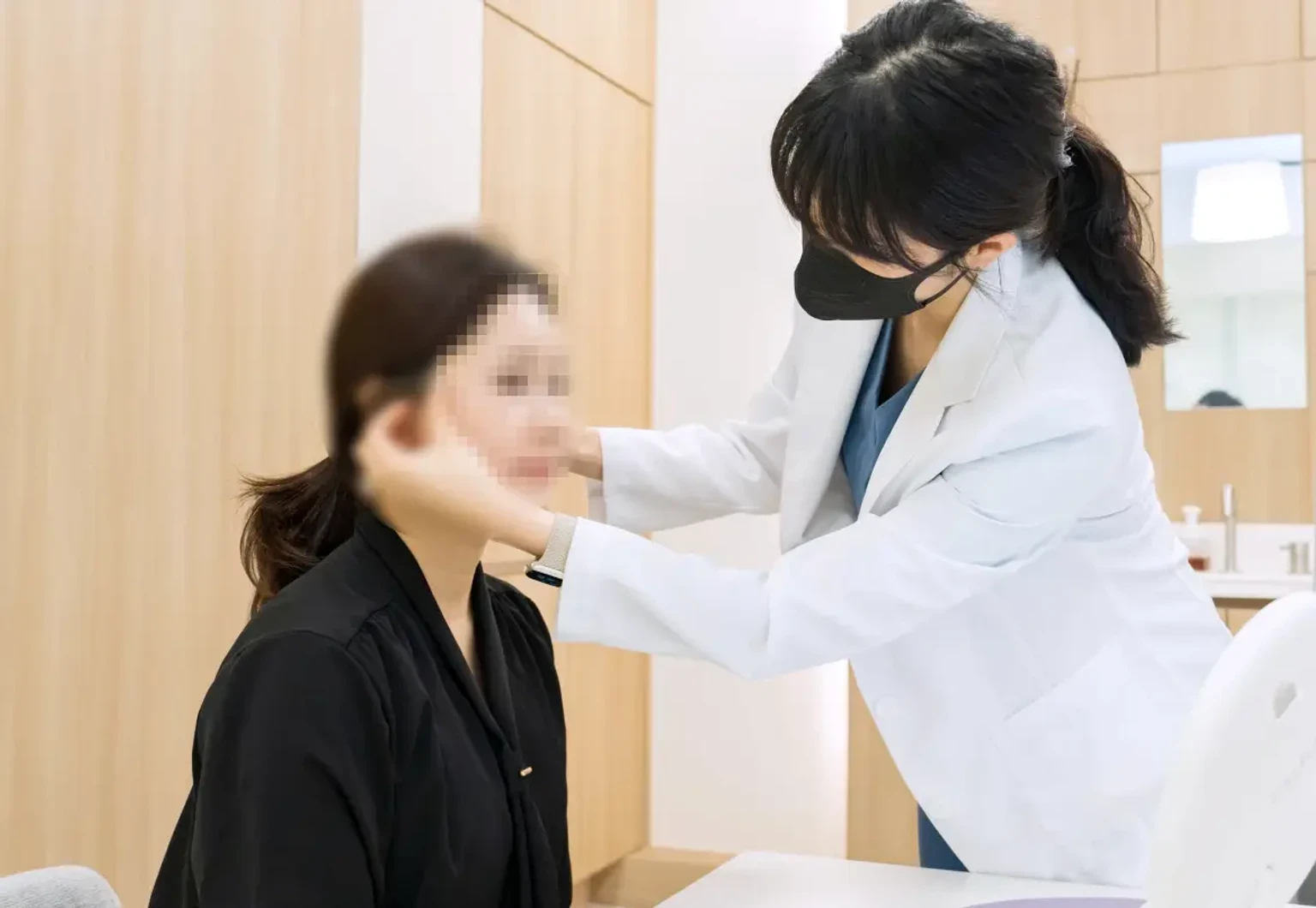 피부과 진료실에서 흰 가운과 마스크를 착용한 의료진이 환자의 얼굴 피부 상태를 살펴보며 상담하는 모습.