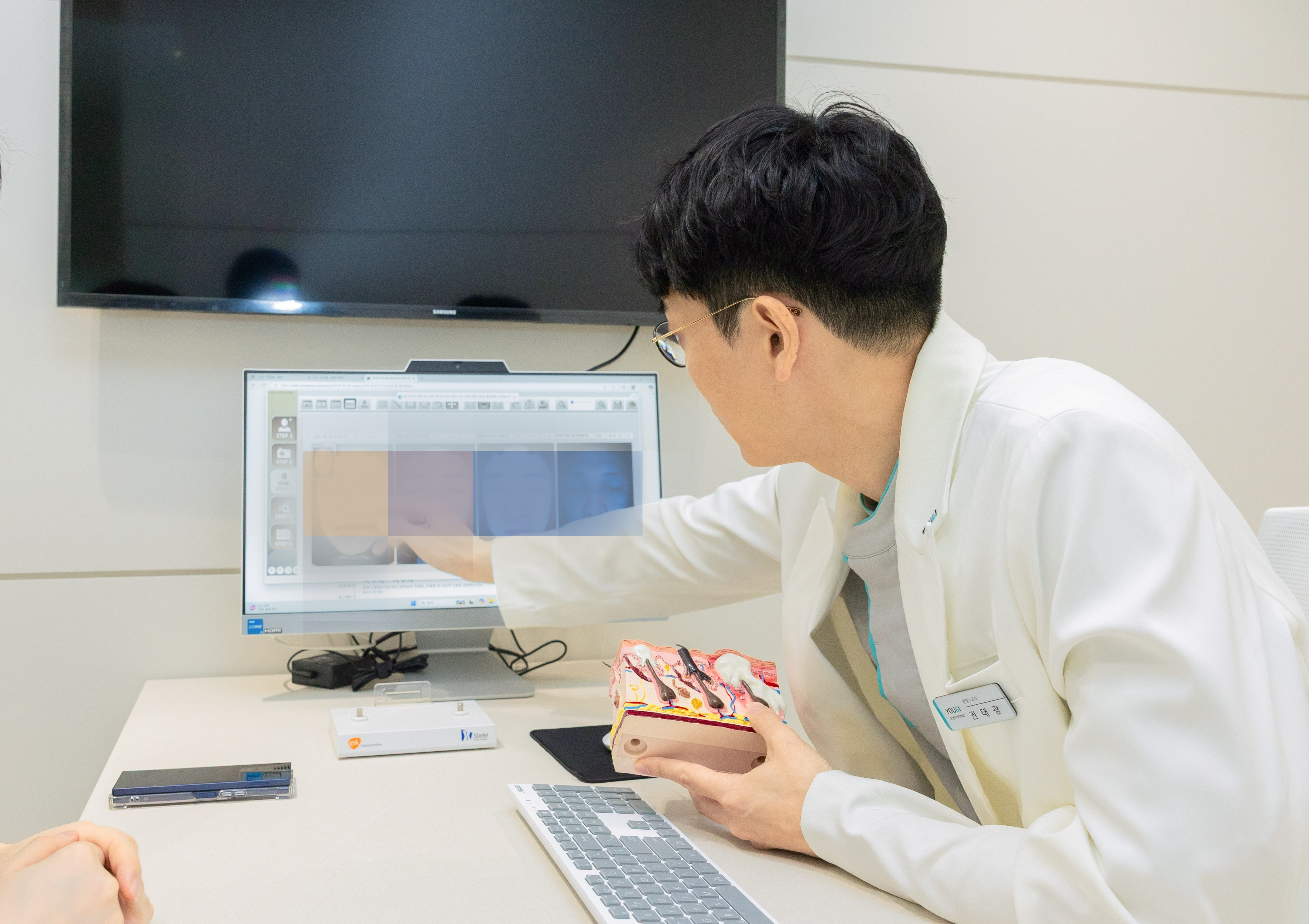 유앤아이피부과의원 분당미금점 권태광 원장이 피부 단면 모형과 모니터를 활용해 피부 상태와 시술 방향을 설명하는 모습