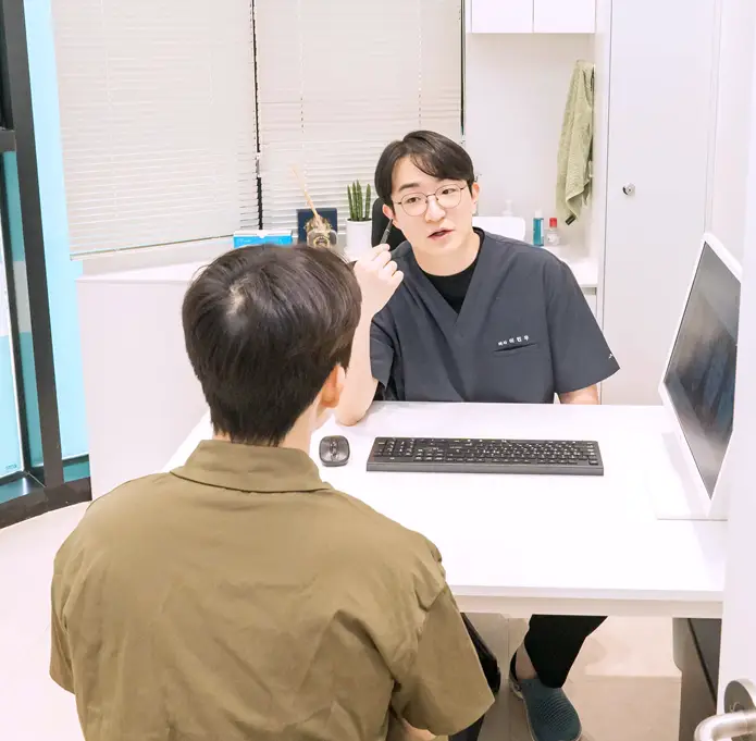 피부과 진료실에서 의료진이 환자와 일대일 상담을 진행하는 모습. 피부 상태와 고민을 확인하고 맞춤형 피부 시술 계획을 설명하는 진료 상담 장면