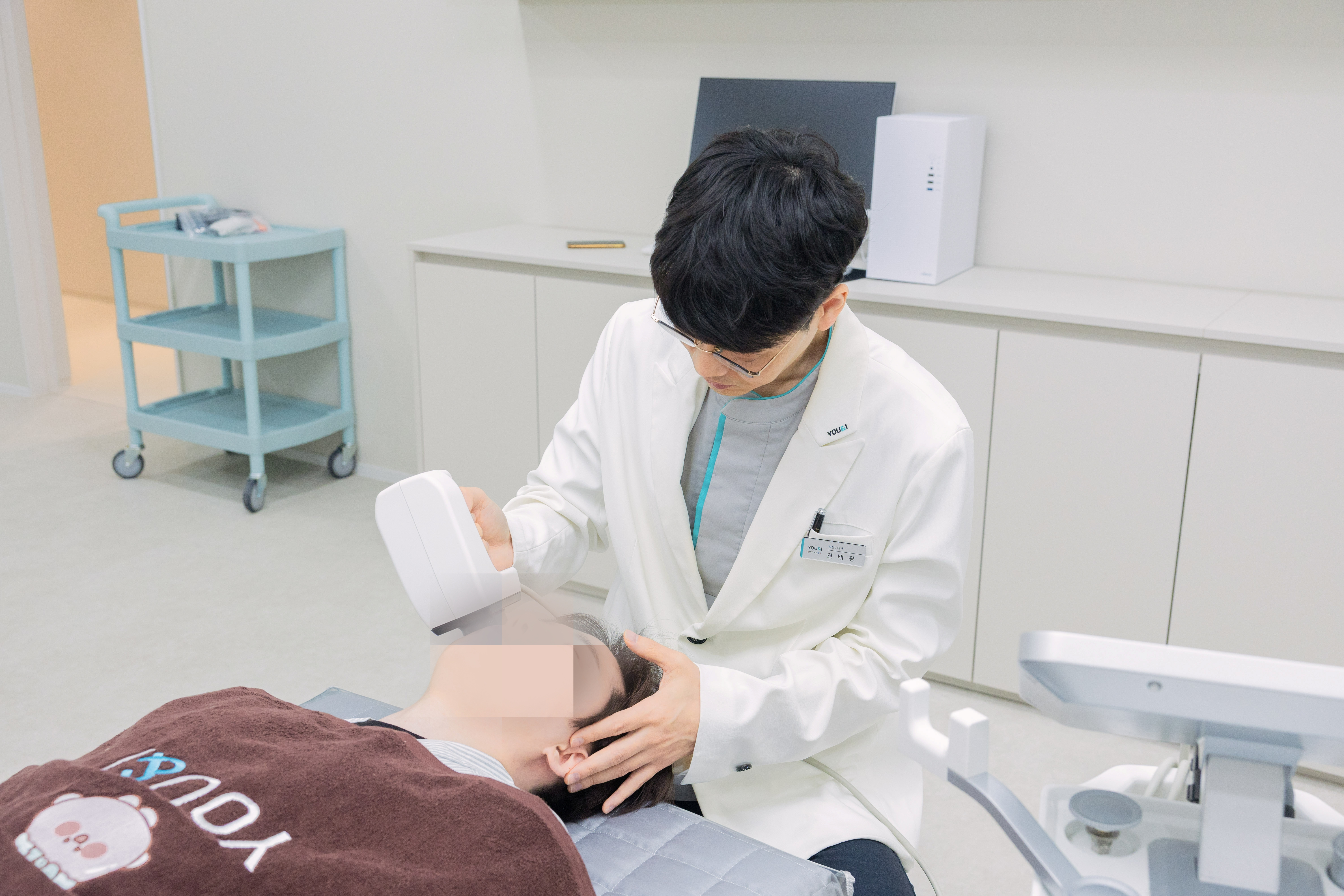 유앤아이피부과의원 분당미금점 권태광 원장이 누워 있는 환자의 얼굴에 핸드피스를 밀착해 시술하는 모습
